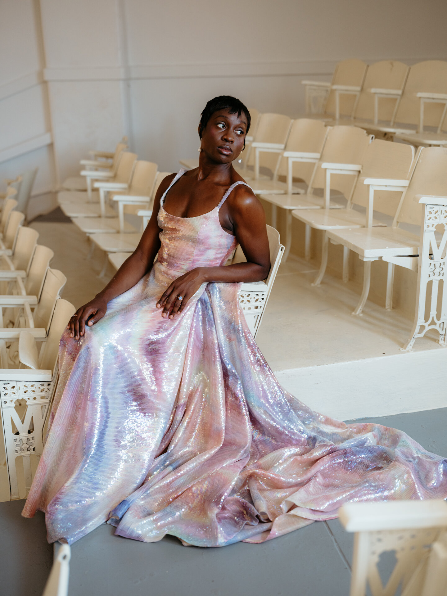 A person sitting on a chair wearing a rainbow beaded Loulette wedding dress.